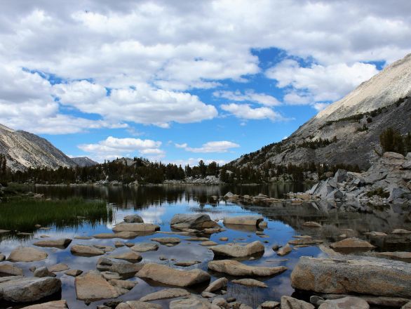 Serene mountain lake with rock reflections under a vibrant blue sky.