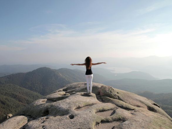 A woman stands and embraces freedom on a mountain peak overlooking a vast landscape.